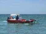 Ein Boot mit großen Rechen, welches das Wasser in Strandnähe von Unrat befreit
